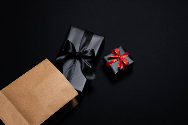 Κάτοψη του κουτιού δώρου με κόκκινη, χάρτινη τσάντα για ψώνια και μαύρες κορδέλες που απομονώνονται σε μαύρο φόντο. Shopping έννοια πυγμαχία ημέρα και μαύρο Παρασκευή πώληση σύνθεση. - Φωτογραφία, εικόνα