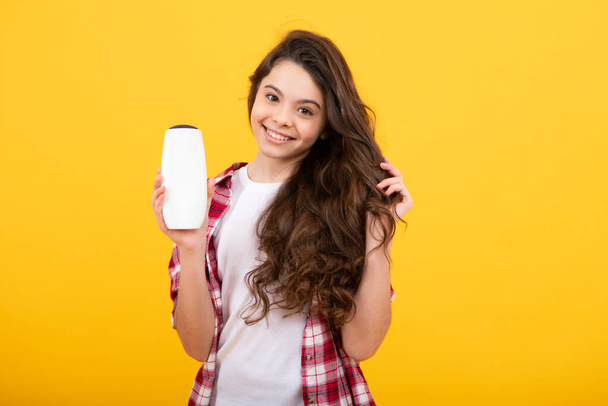 Teenager child girl showing bottle shampoo conditioners or shower gel. Hair cosmetic product. Bottle for advertising mock up copy space. Happy teenager, positive and smiling emotions of teen girl - Photo, Image
