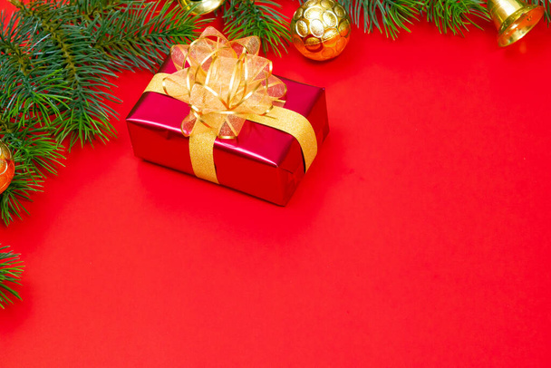Kerst achtergrond concept. Bovenaanzicht van kerst geschenkdoos gouden ballen met sparren takken en bel op rode achtergrond. - Foto, afbeelding