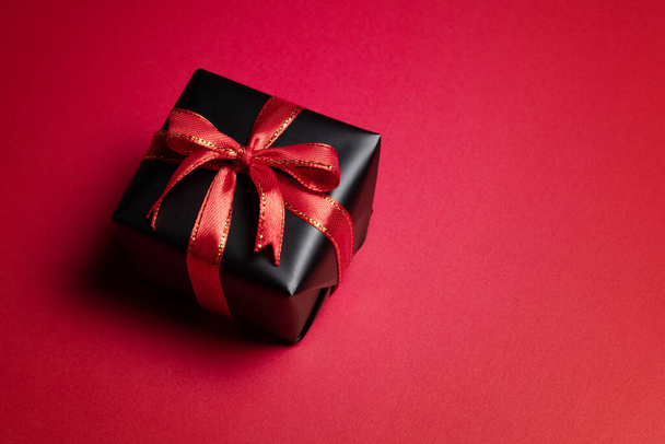 Вид зверху на чорну різдвяну подарункову коробку з червоними та чорними стрічками ізольовано на червоному тлі. Концепція шопінгу різдвяний день, день Святого Валентина і чорна п'ятниця продаж композиції
. - Фото, зображення