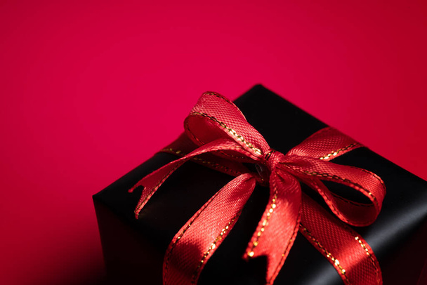 Вид зверху на чорну різдвяну подарункову коробку з червоними та чорними стрічками ізольовано на червоному тлі. Концепція шопінгу різдвяний день, день Святого Валентина і чорна п'ятниця продаж композиції
. - Фото, зображення