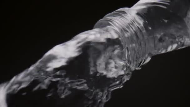 Mineraalwater gieten flessenhals in super slow motion close-up. Snelle stroom van heldere vloeistof stroomt naar beneden uit glazen container op zwarte achtergrond. Verse biologische drank voor een gezond energieleven. - Video