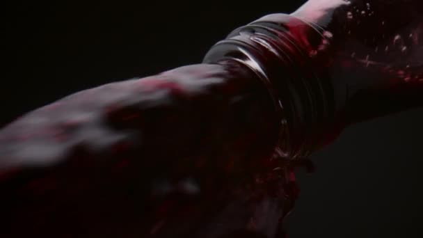 Stream of red wine pouring out from bottle neck close up. Fresh alcohol drink outflowing from glass container on black background. Stormy jet of delicious merlot falling down in super slow motion. - Footage, Video