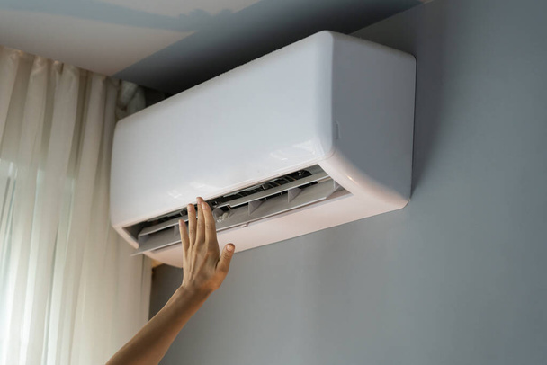 Female owner of apartment stretches hand to check operating air conditioner and catch stream of warm air. Person wants to make flat warm turning on modern device. Landlady enjoys caring about house - Photo, Image