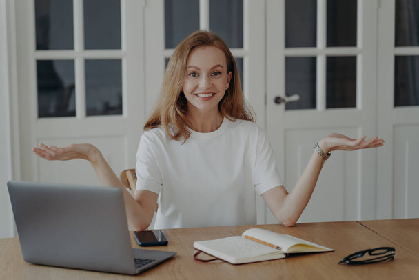 Woman is happy and puzzled. Successful mid adult businesswoman is working from home. Lovely european lady in white t-shirt is freelancer having remote work in her apartment. Concept of work easiness. - Φωτογραφία, εικόνα