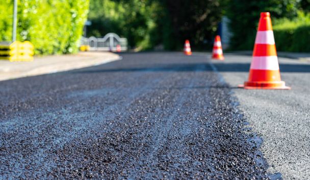 Construction cones marking part of road with a layer of fresh asphalt.	 - Foto, Imagen