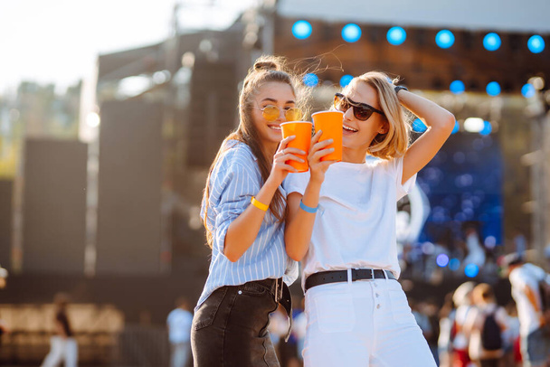 Two female friends drink beer and have fun at the music festival.  Summer holiday, vacation concept. - Фото, зображення