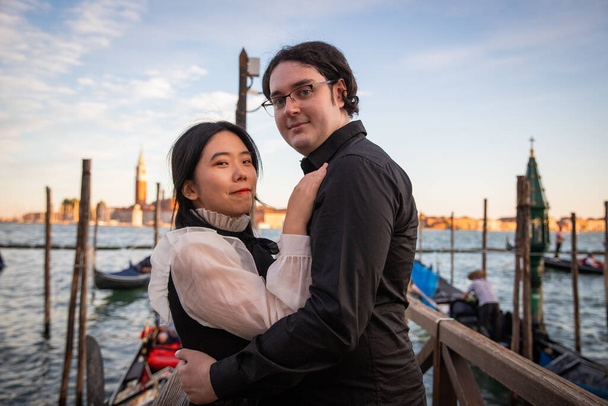 Young multi-ethnic couple embraced in front of canal and near gondoliers. - Photo, Image