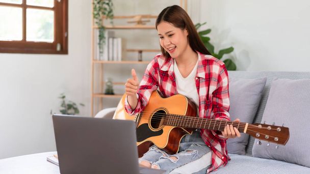 Hobby έννοια, νεαρή Ασιάτισσα γυναίκα παίζει ακουστική κιθάρα σε ζωντανή μετάδοση και κάνει αντίχειρες προς τα πάνω χειρονομία. - Φωτογραφία, εικόνα