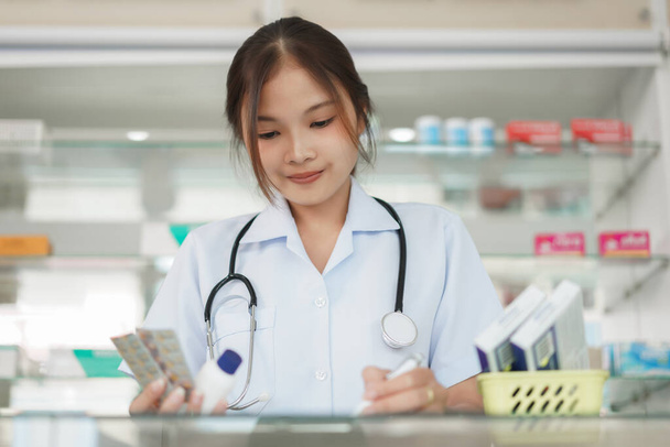 Medicine and health concept, Female pharmacist hold pill bottle and capsule to writing prescription. - 写真・画像
