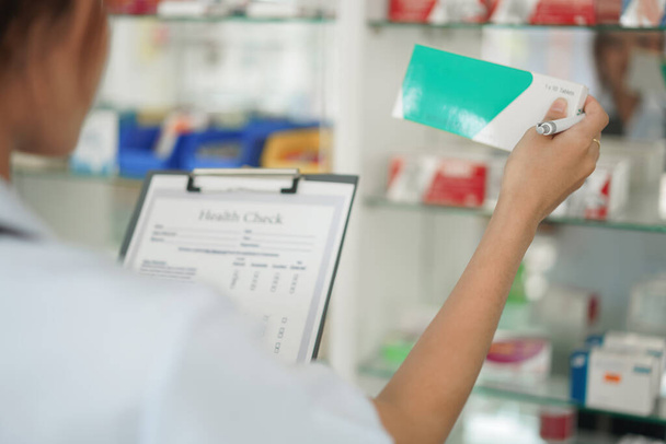 Medicine and health concept, Female pharmacist hold medicine box to checklist in paper at drugstore. - Foto, afbeelding