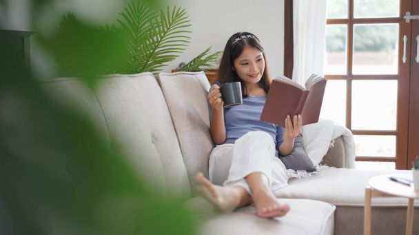 Робота з домашньої концепції, ділові жінки читають книгу і п'ють каву, лежачи на дивані, щоб розслабитися
. - Фото, зображення
