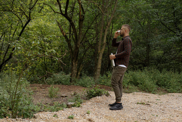 mężczyzna spaceruje po lesie, odpoczywa i pije drinka z termosu - Zdjęcie, obraz