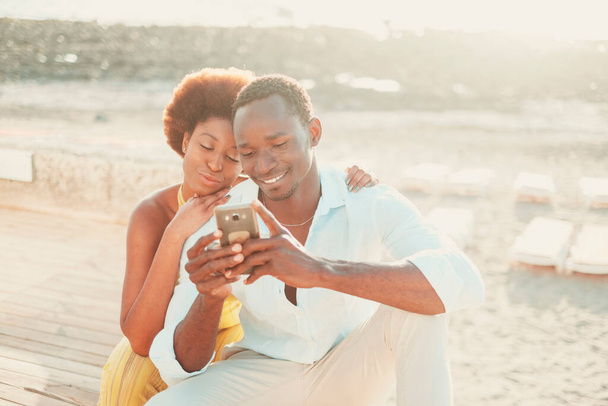 Coppia nera giovane uomo e donna godono insieme la tecnologia di connessione utilizzando il telefono cellulare e l'app. Happy persone moderne che scrivono su smartphone in attività ricreative all'aperto insieme sorridendo e divertendosi - Foto, immagini