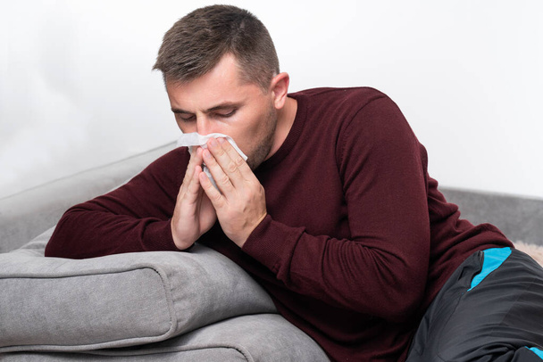 Αδύναμος και κουρασμένος άνθρωπος φυσάει τη μύτη του σε ένα μαντήλι, αλλεργία και καταρροή μύτη σε έναν άνδρα. - Φωτογραφία, εικόνα