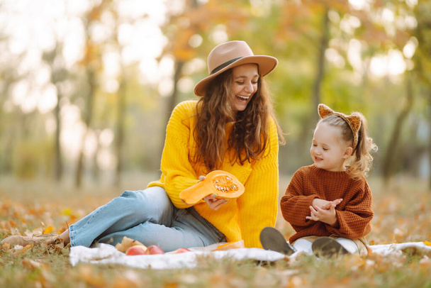 Fall picnic with pumpkin. Young mother and cute daughter resting in nature. Autumn harvest. Childhood. - Foto, imagen