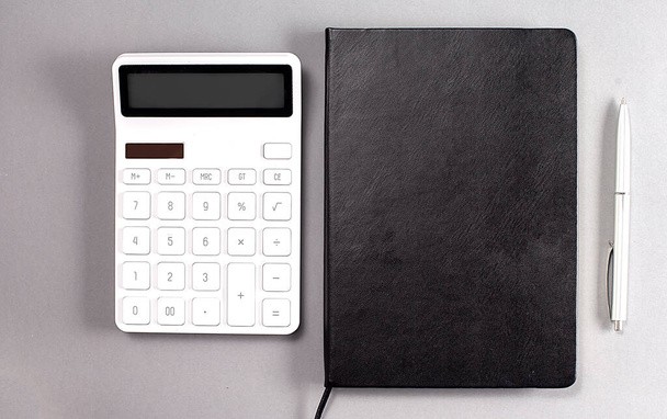 Black notebook and calculator and pen on a grey background - Фото, зображення