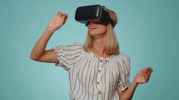 Femme adulte incroyable en chemise en utilisant casque casque app pour jouer à un jeu de simulation. Regarder la vidéo 3D 360 de réalité virtuelle. Jeune fille en lunettes VR isolé sur fond bleu. La dépendance aux nouvelles technologies - Photo, image