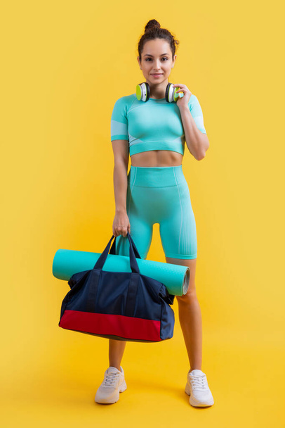 positive fitness woman in sportswear with sport bag in studio. fitness woman in sportswear isolated on yellow background. fitness and sportswear. - Zdjęcie, obraz