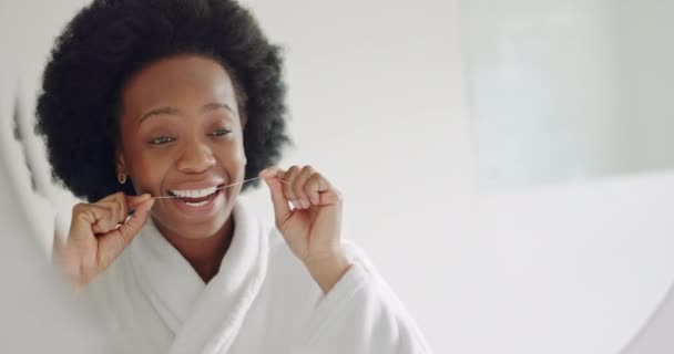 Spiegel, tandzijde en tanden gezondheidszorg zwarte vrouw schoonmaken mond voor gezonde tandvlees, glimlach en frisse adem. Afrikaanse persoon in de badkamer met tandheelkundige gezondheid of tandheelkundige hygiëne ochtend douche routine. - Video