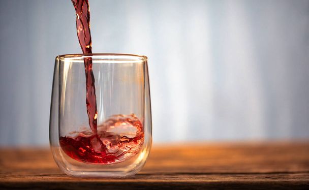 Red liquid, juice or wine is poured into a glass. - Zdjęcie, obraz