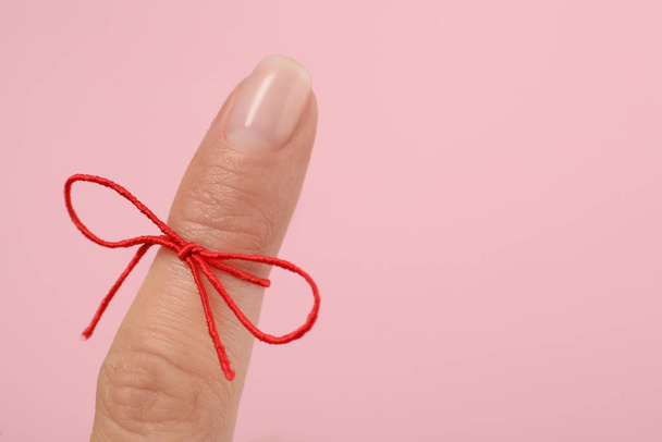Woman showing index finger with tied red bow as reminder on pink background, closeup, Space for text - Φωτογραφία, εικόνα