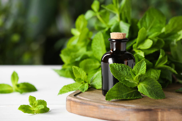 Butelka miętowego olejku eterycznego i zielone liście na białym drewnianym stole, zbliżenie. Miejsce na tekst - Zdjęcie, obraz