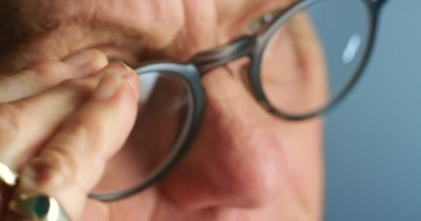 Bril, gezichtsvermogen en gezicht van een senior die een nieuwe bril, bril of bril uitprobeert. Zoom macro, ogen of gezichtsvermogen van gepensioneerde mensen met voorgeschreven lenzen op blauwe achtergrond. - Video