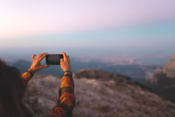 beautiful young girl travels and takes a photo on the phone. travel in the mountains. portrait of a girl with a phone at sunset. - Foto, afbeelding