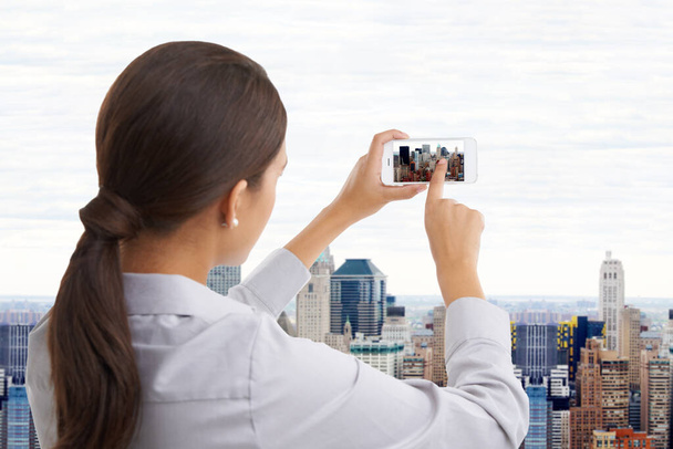 The city I live in. Rearview shot of a businesswoman taking a photo of a cityscape through a window - 写真・画像