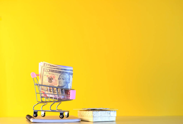 carrito de compras con dinero y monedas sobre fondo amarillo - Foto, imagen