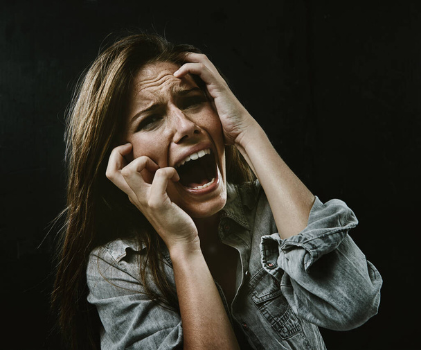 Het gezicht van wanhoop. Een jonge vrouw schreeuwen ongecontroleerd terwijl geïsoleerd op een zwarte achtergrond - Foto, afbeelding