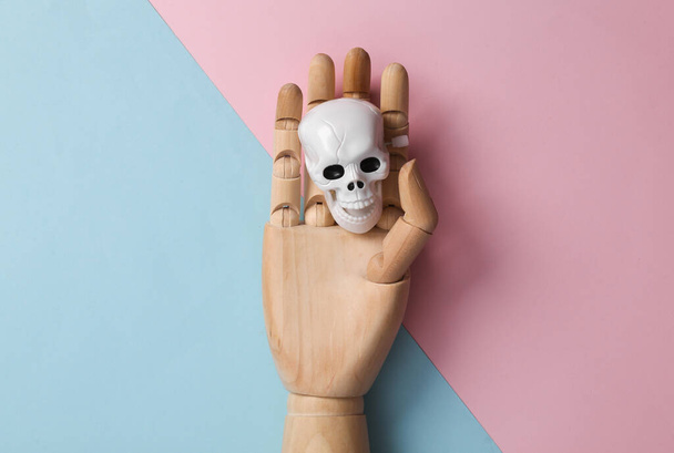 Wooden hand with a skeleton head on a blue pink background. Minimal halloween layout. Top view. flat lay - Fotoğraf, Görsel