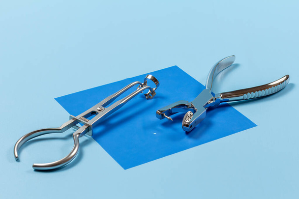 Dental hole punch and a rubber dam forceps with the clamp on the blue rubber dam. Medical tools concept. - Photo, Image