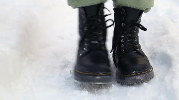 Vorderansicht eines gefrorenen stehenden Mannes in schwarzen Stiefeln im Winter. Zeitraffer des Schüttelns von Schnee aus Stiefeln im Winter am Hauseingang. Schnee von den Schuhen abschütteln, starker Schneefall im Winter. - Filmmaterial, Video
