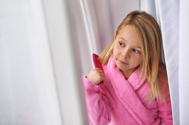 Kids have it easy. a young girl in a bathrobe combing her hair - Foto, Imagen
