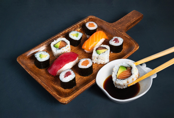 Maki-Sushi-Brett mit Sojabohnenschale und Essstäbchen, die ein Stück eintauchen - Foto, Bild