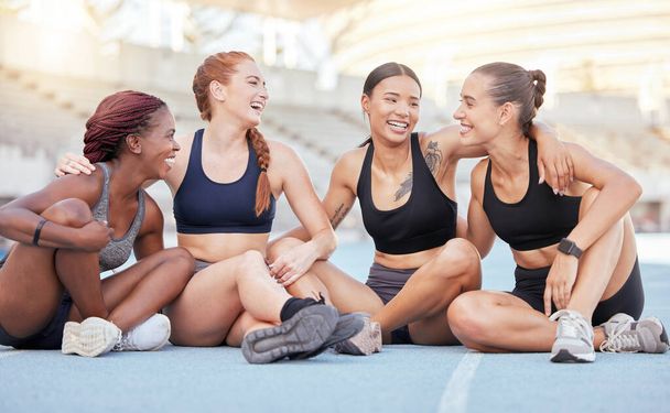 Happy, diversity and sports women, friends and athletes break from marathon training workout on running track at stadium arena outdoors. Smile, healthy and fitness group rest, motivation and support. - Photo, Image
