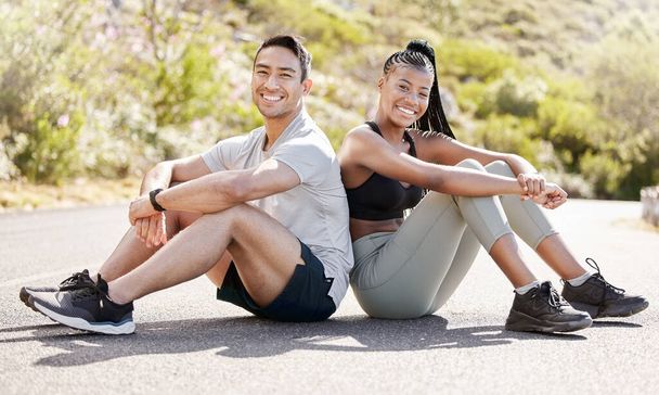 Portrait of couple resting in the street after workout, running and exercise. Young, smiling and multicultural couple sitting on the road after a run, training or exercising together in urban city. - Foto, imagen