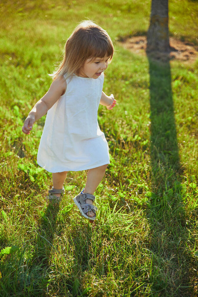 encantador niño en vestido de lino caminando por el césped. - Foto, imagen