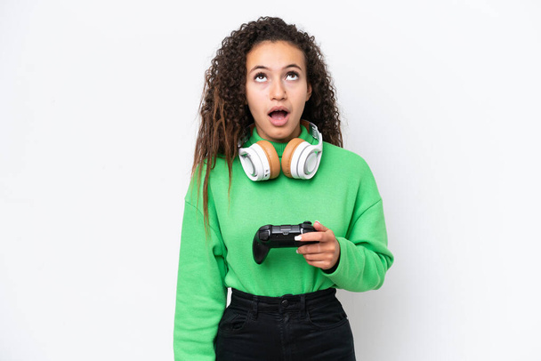 Young Arab woman playing with a video game controller isolated on white background looking up and with surprised expression - Valokuva, kuva