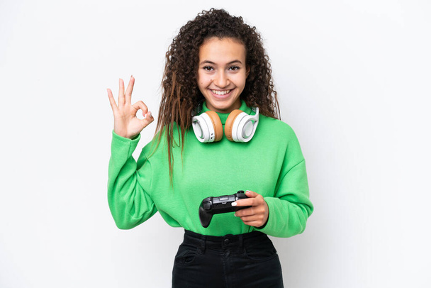 Junge Araberin spielt mit einem Videospiel-Controller auf weißem Hintergrund, der Ok-Zeichen mit den Fingern zeigt - Foto, Bild