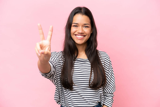 Young Colombian woman isolated on pink background smiling and showing victory sign - Photo, Image