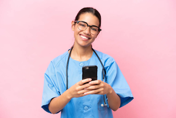 Jeune infirmière colombienne isolée sur fond rose envoyant un message avec le mobile - Photo, image