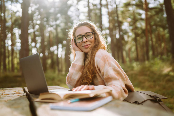 Beautiful woman working online or studying at laptop sitting at park. Business, blogging, freelance, education concept. - Foto, Imagem
