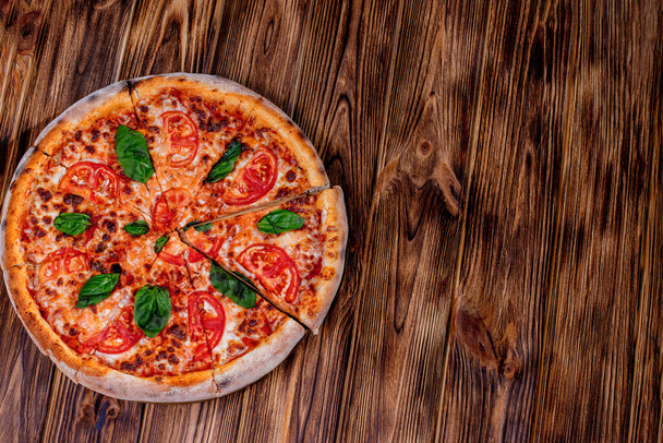 Delicious fragrant pizza-Margherita with mozzarella, tomatoes and basil on tomato sauce on woden background. Copy space. - Foto, Bild