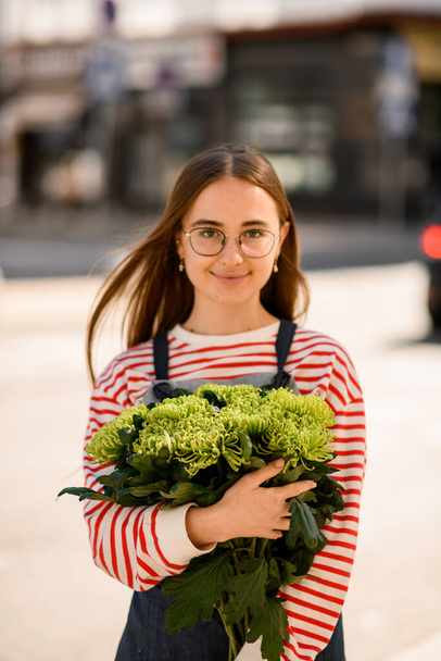 great portrait of attractive young woman in glasses with long hair holding bouquet of fresh green chrysanthemum flowers in her hands - Photo, Image