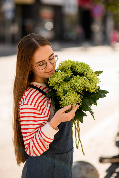 beautiful young woman in glasses with long hair holds bouquet of fresh green chrysanthemum flowers in her hands - Foto, afbeelding