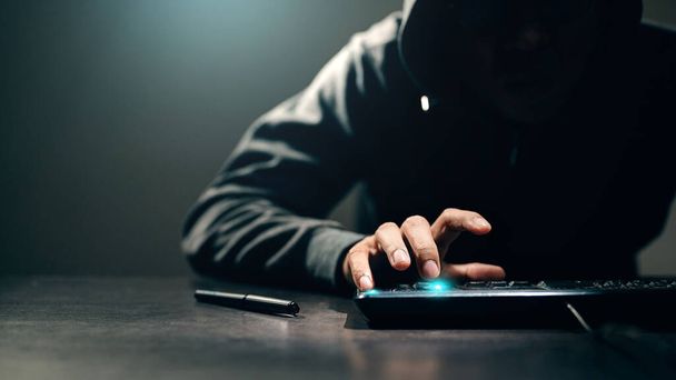 Hacker, ladrón está utilizando la tecla del teclado para romper los códigos de defensa o disparar virus en la computadora. Los alrededores estaban llenos de oscuridad y camuflaje para esconderse. - Foto, imagen