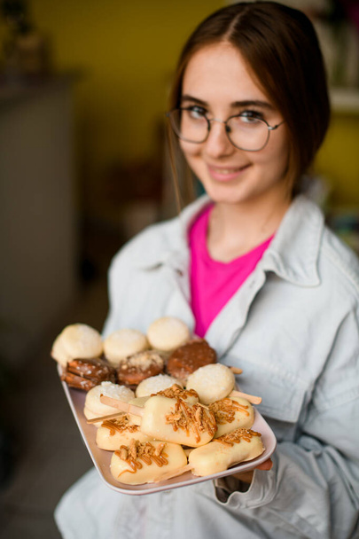 delicious sweet macarons covered with chocolate icing on tray in hands of pretty smiling woman. Dessert in the form of ice cream with stick - Фото, зображення